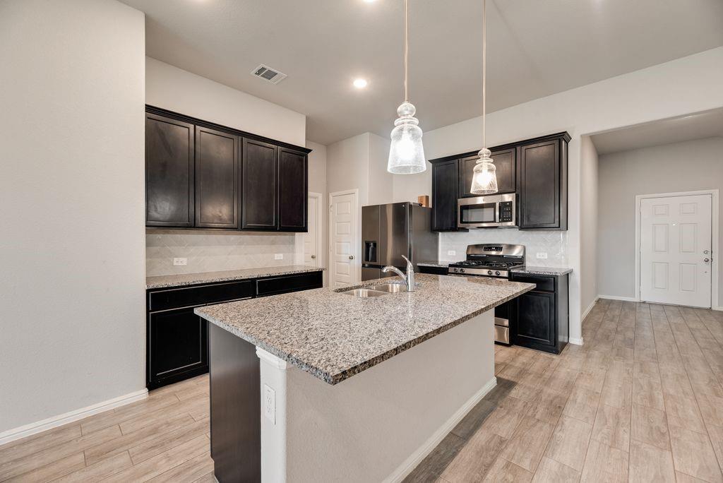 14216 Aberavon Drive Pilot Point, TX 76258 - Photo 7 of 19 Kitchen with granite countertops, dark wood cabinetry, stainless steel appliances, and wood-look flooring