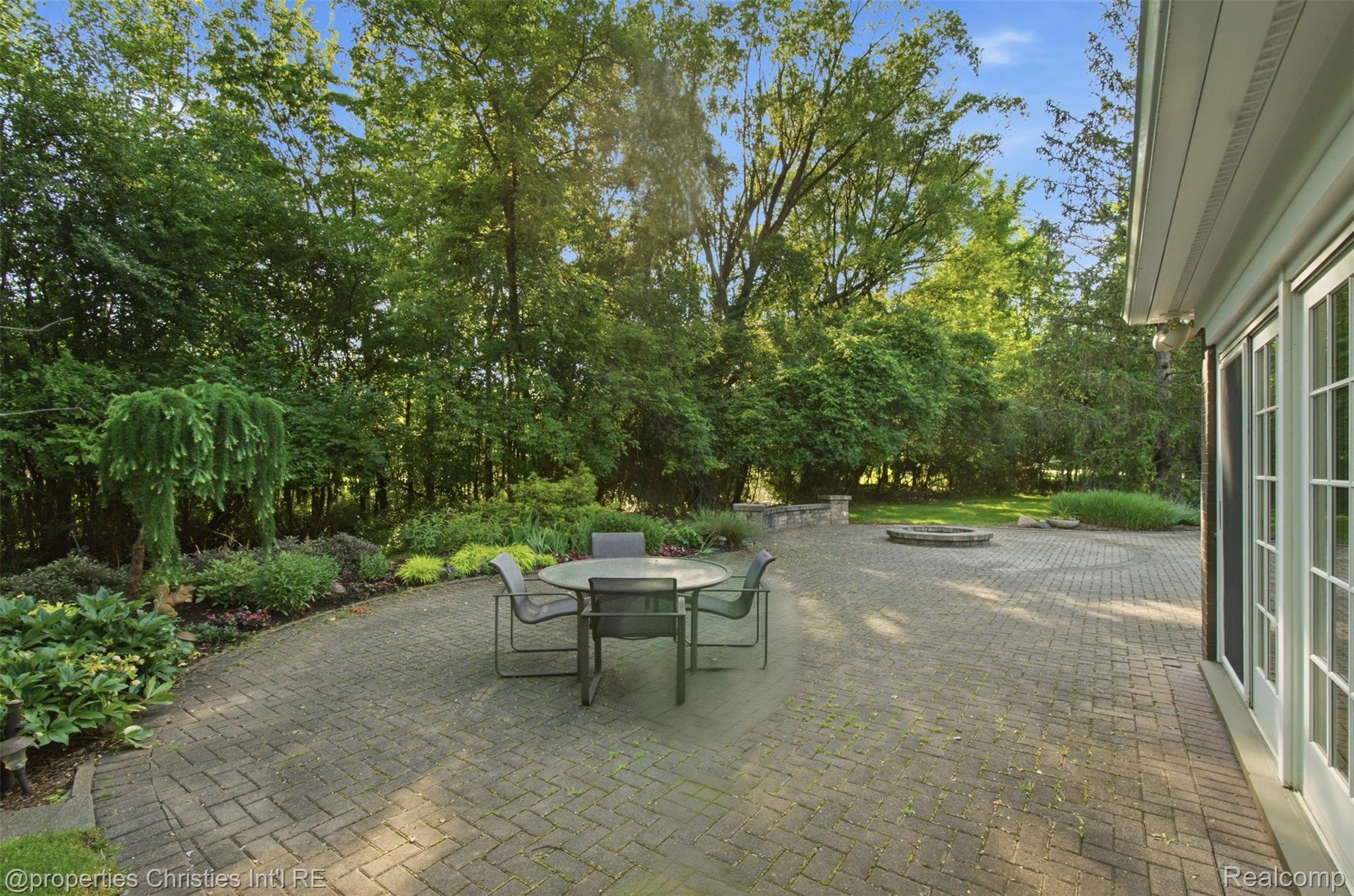 25235 Canterbury Road Franklin, MI 48025 - Photo 46 of 56 Expansive paver patio with a stone fire pit, bordered by mature trees and lush landscaping