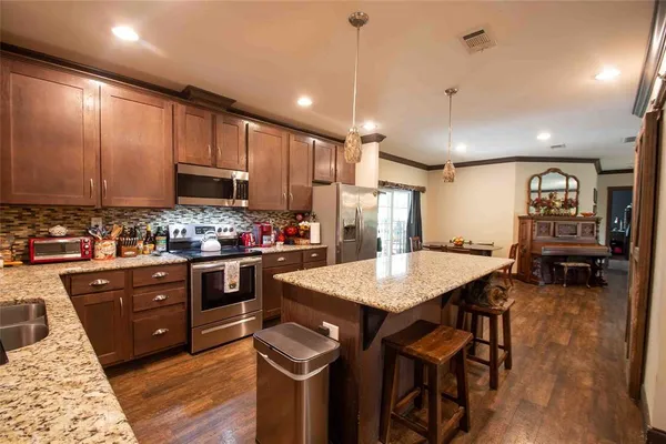 a kitchen with stainless steel appliances kitchen island granite countertop a refrigerator a stove a sink a dining table and chairs with wooden floor