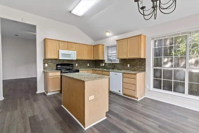 a kitchen with granite countertop a stove a sink dishwasher and a microwave oven with wooden floor