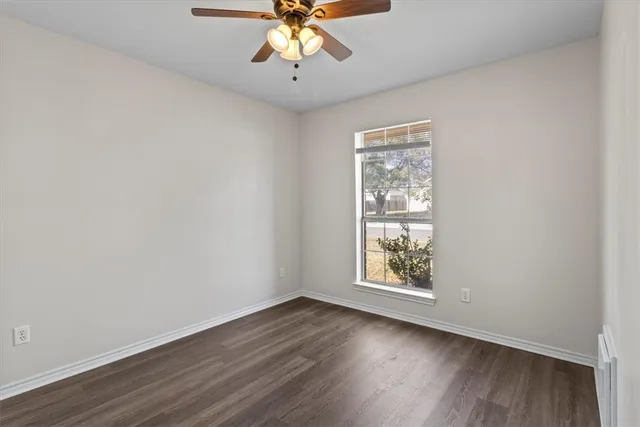 an empty room with wooden floor chandelier fan and windows