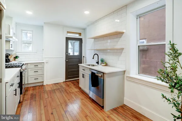 a kitchen with a hard wood floor white cabinets and stainless steel appliances