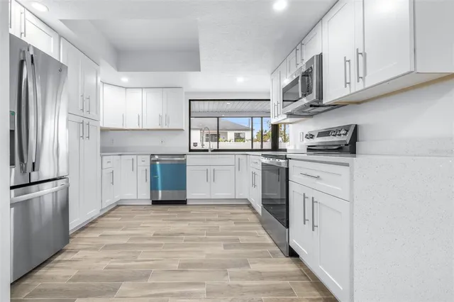 a kitchen with stainless steel appliances granite countertop white cabinets a sink a stove a microwave and oven with wooden floor