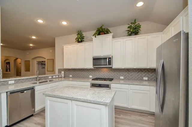 a kitchen with granite countertop a sink stainless steel appliances and white cabinets