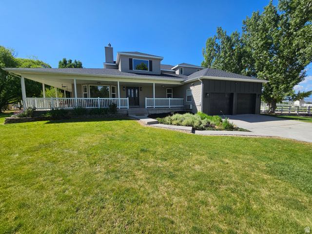 812 East Bates Cyn Road Tooele, UT 84074 - Photo 133 of 144 Contemporary two-story residence featuring a covered wrap-around porch with white railings, an attached two-car garage with dark paneled doors, and a paved driveway
