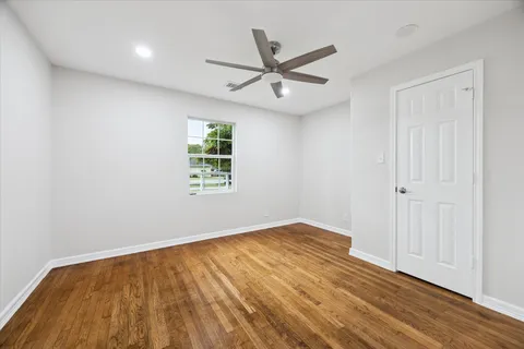 an empty room with wooden floor ceiling fan and windows
