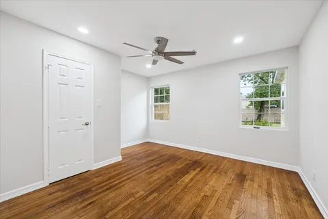 an empty room with wooden floor ceiling fan and windows