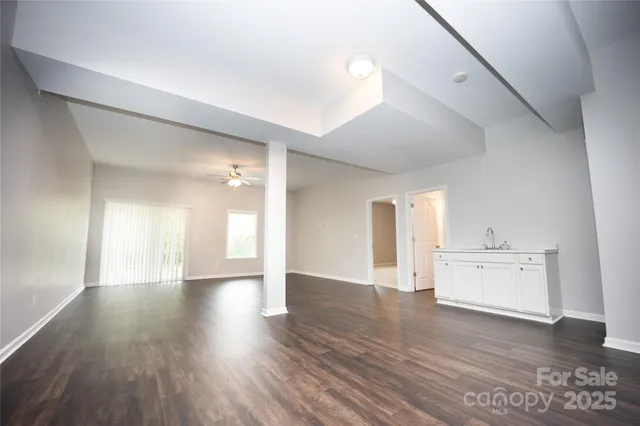 a view of an empty room and a kitchen with wooden floor