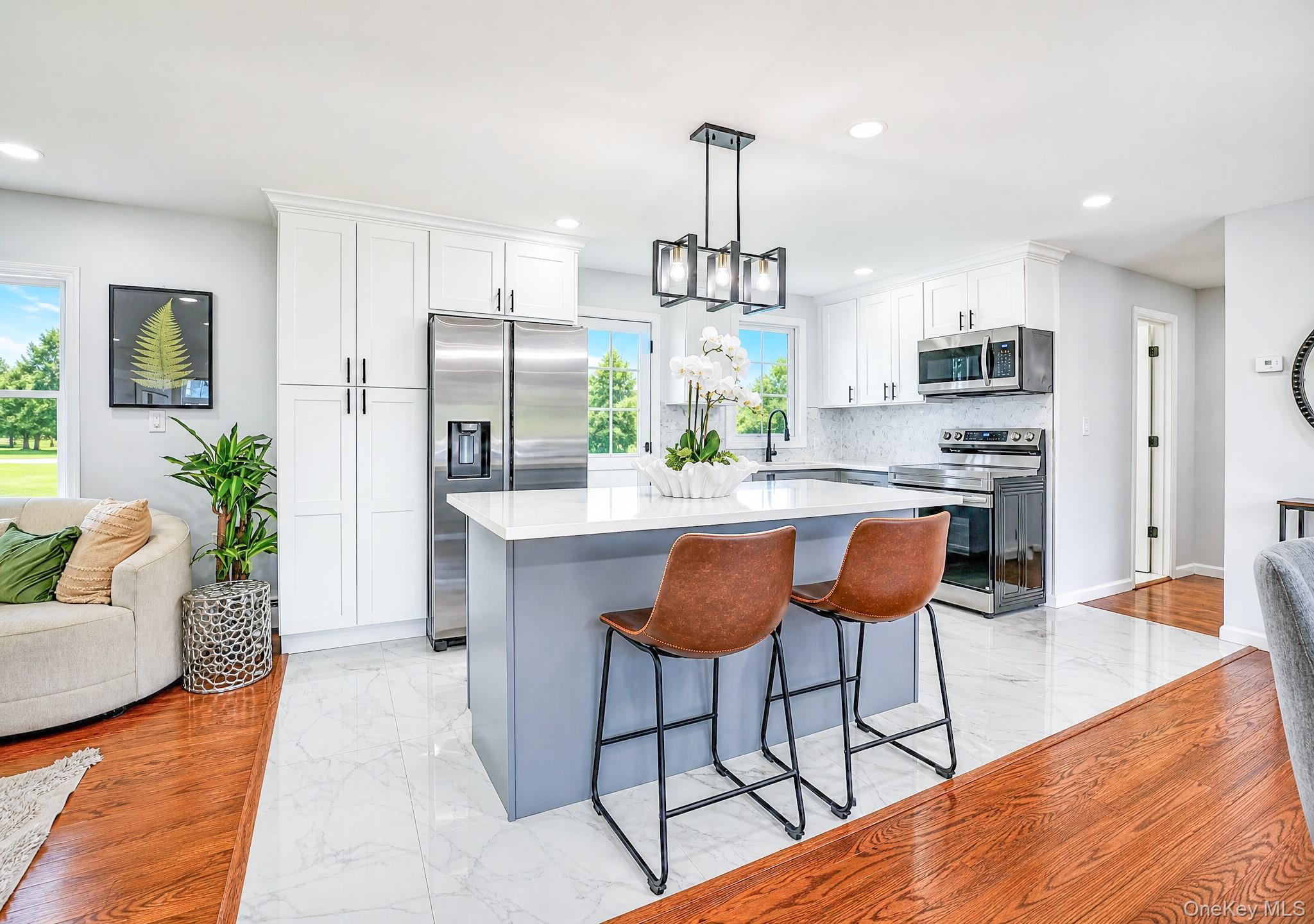 61 Cheshire Road Bethpage, NY 11714 - Photo 9 of 25 Modern kitchen featuring a central island with a light countertop, white shaker cabinetry, stainless steel appliances, and a mosaic tile backsplash