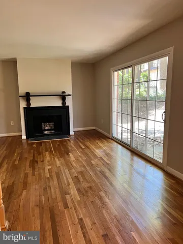 a view of an empty room with wooden floor fireplace and a window