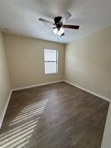 an empty room with wooden floor chandelier fan and windows