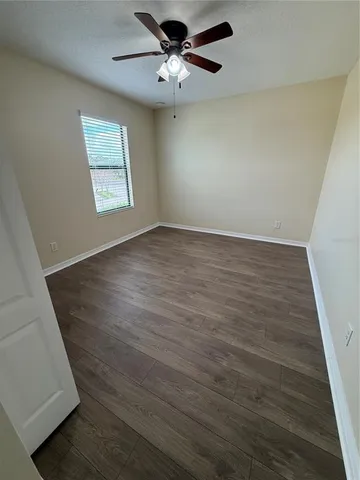 an empty room with wooden floor chandelier fan and windows