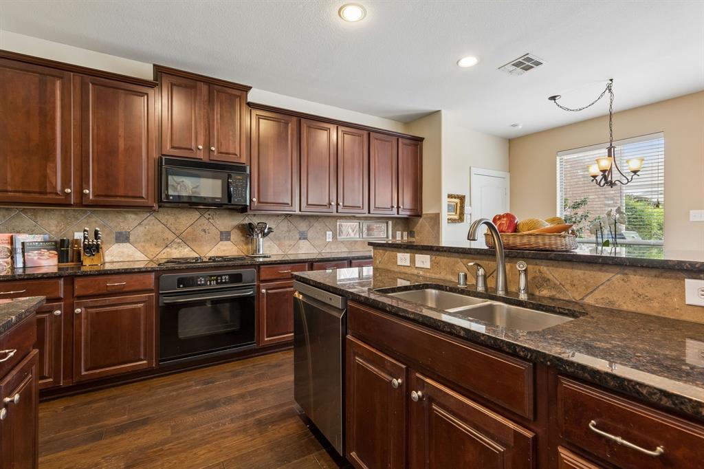960 Remuda Road Frisco, TX 75033 - Photo 11 of 39 Kitchen featuring dark wood cabinetry, a double basin stainless steel sink, dark speckled countertops, and a tiled backsplash