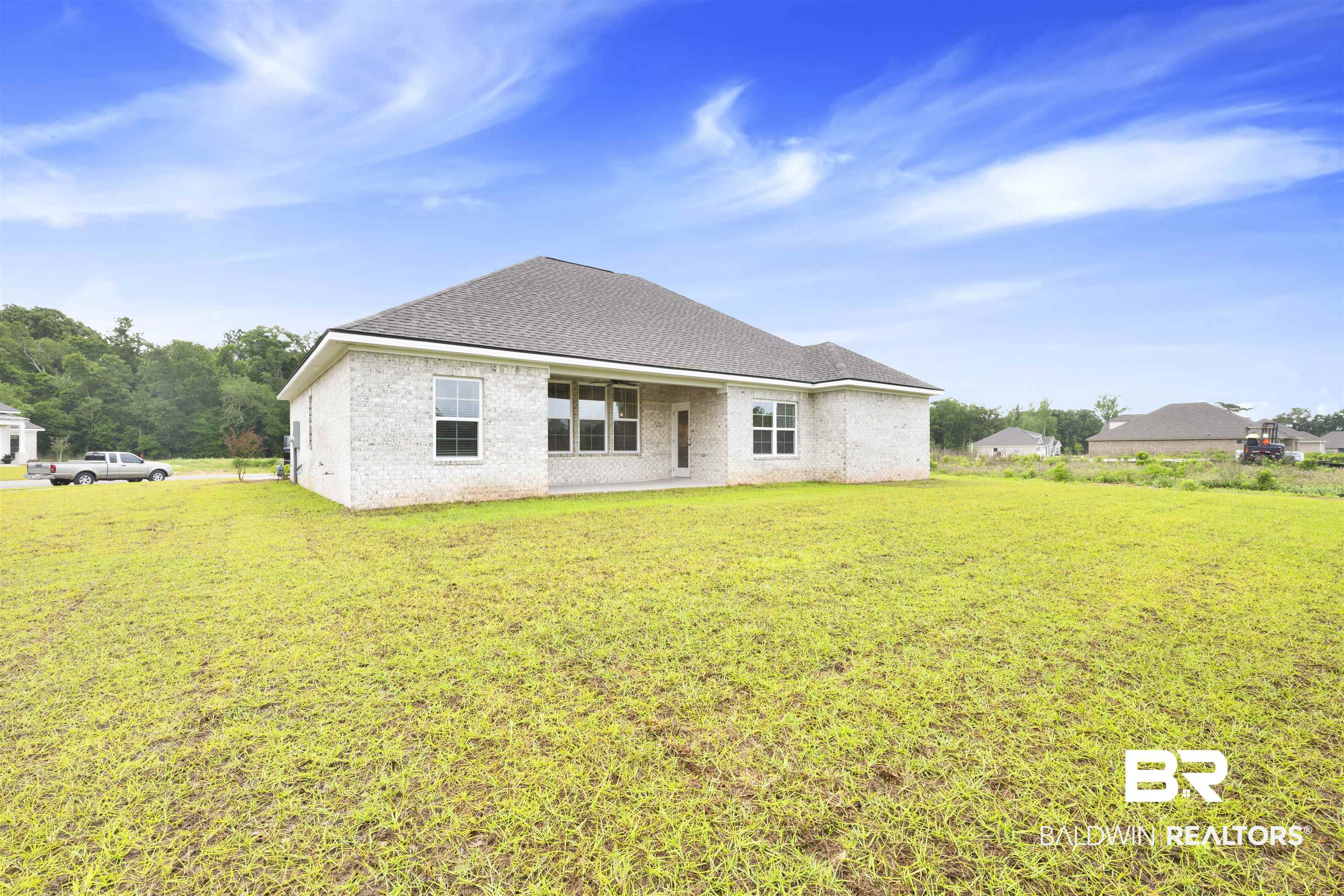 27371 Patch Pl Loop Daphne, AL 36526 - Photo 62 of 63 Expansive green lawn surrounds a contemporary residence featuring light-colored brick siding, a dark shingle roof, multiple windows, and a rear patio