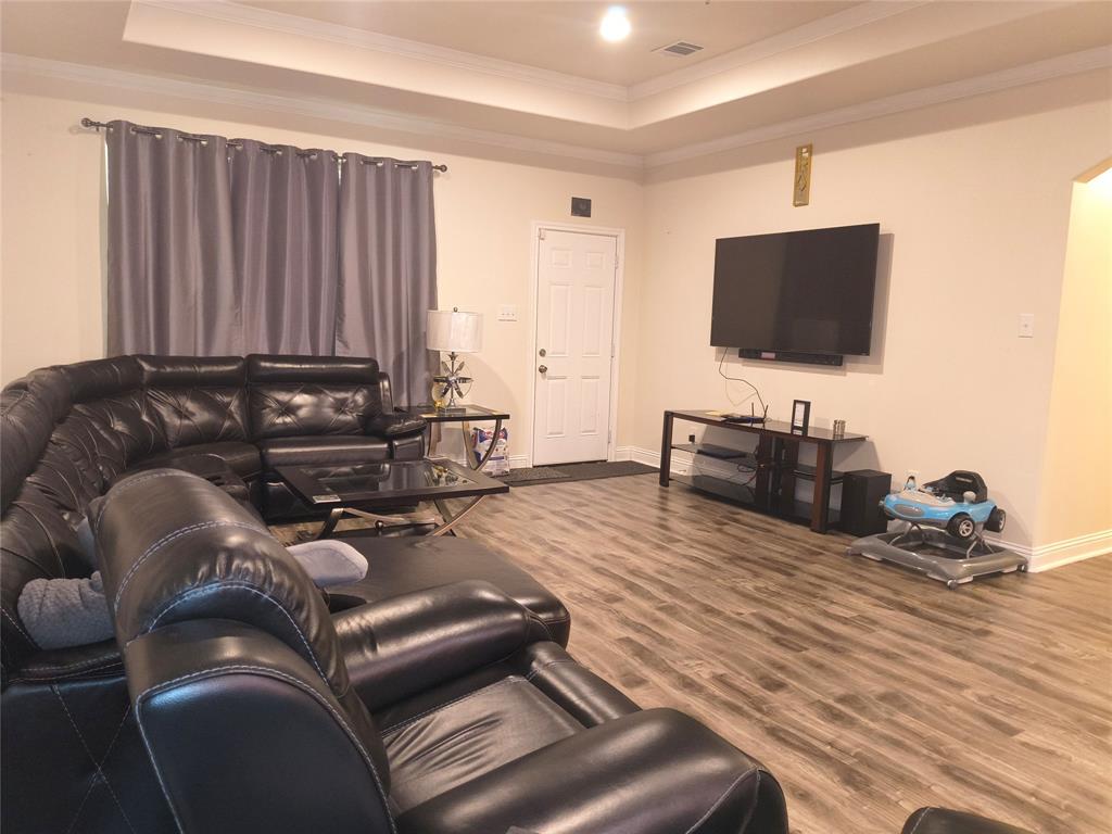 Spacious living area featuring wood-finish flooring, a tray ceiling, and crown molding