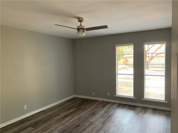 an empty room with wooden floor fan and windows