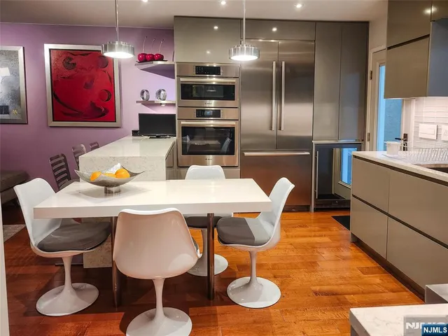 a kitchen with stainless steel appliances kitchen island granite countertop a dining table chairs and a refrigerator