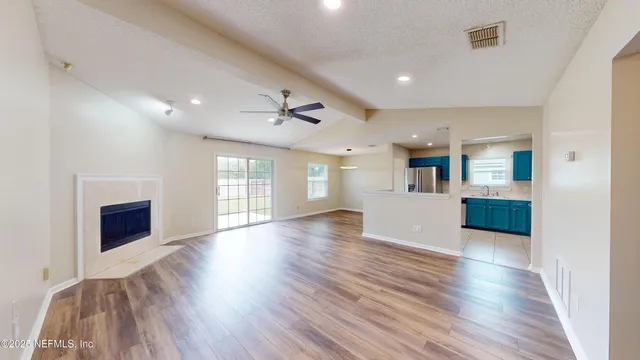 a view of an empty room with wooden floor and a kitchen