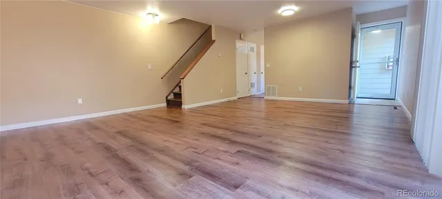 a view of an empty room with wooden floor and stairs