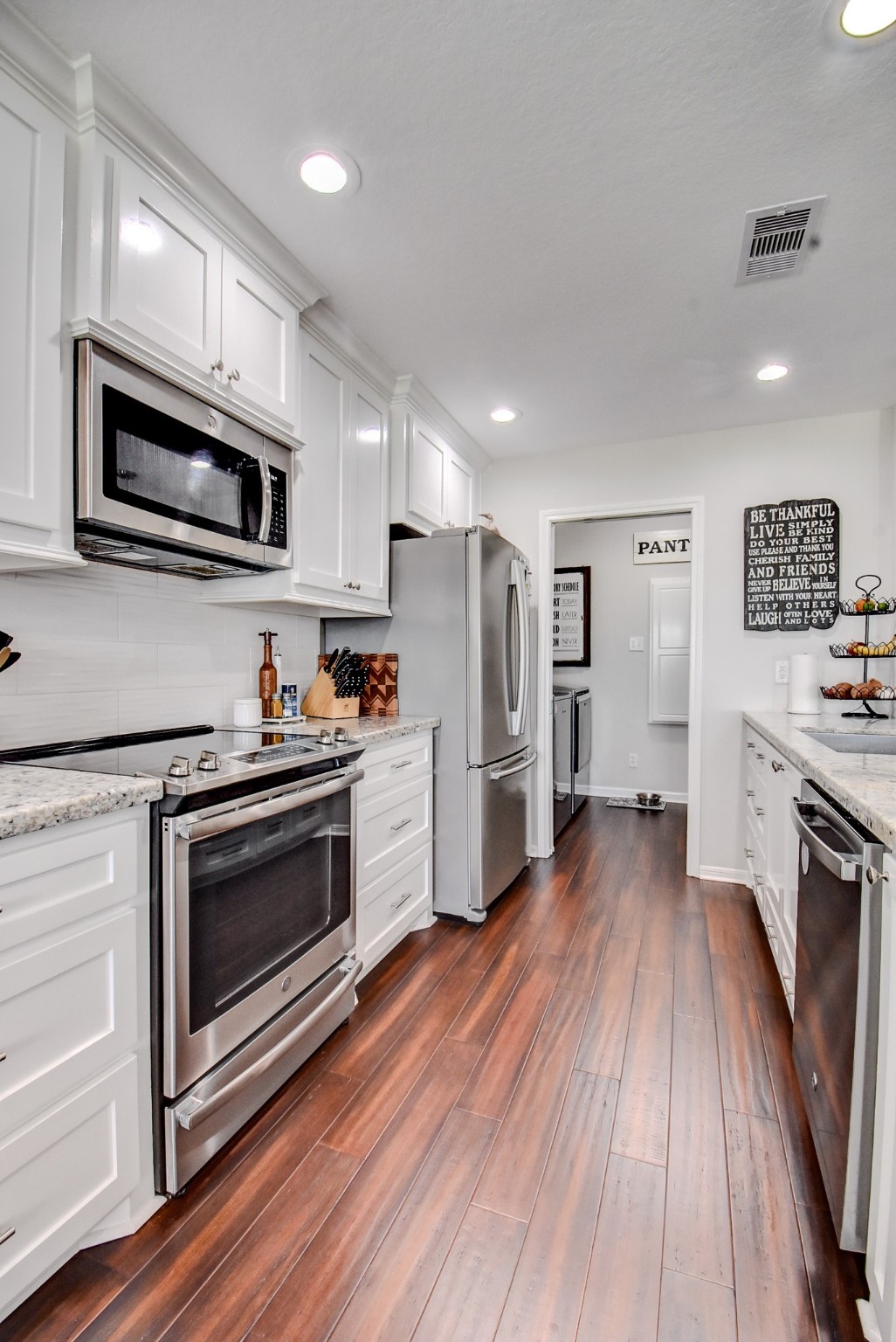122 Four Master Road Freeport, TX 77541 - Photo 19 of 50 a kitchen with stainless steel appliances white cabinets a stove a microwave and wooden floors