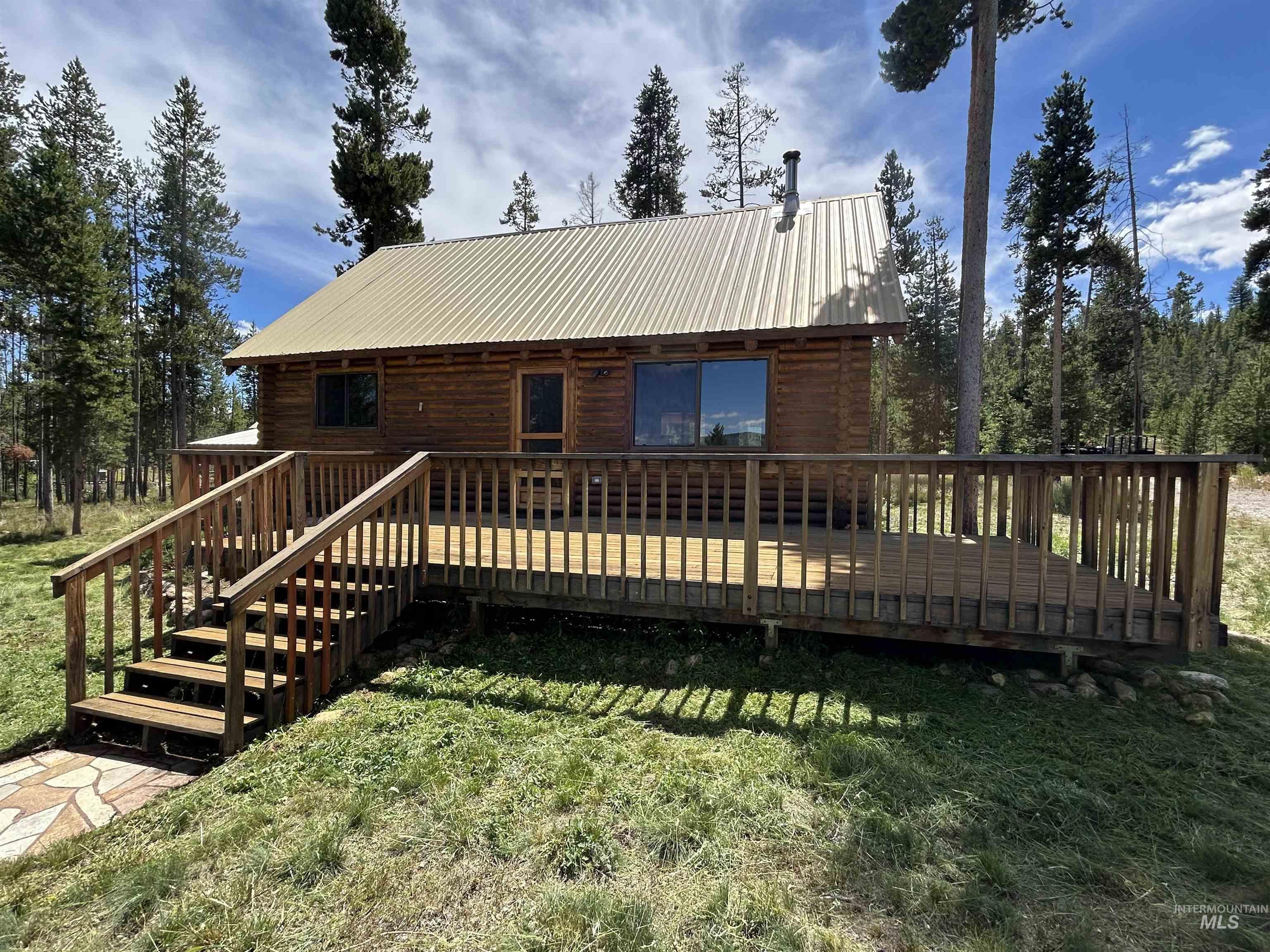 35 Sawtooth Way Stanley, ID 83278 - Photo 1 of 36 Log cabin exterior featuring a spacious wooden deck with railings, a metal roof, and a stone-patterned walkway