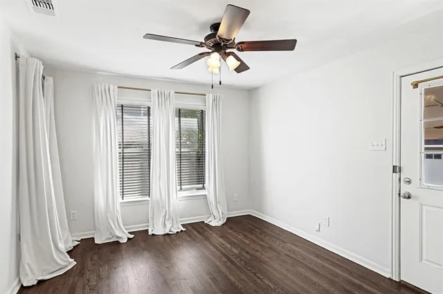 an empty room with wooden floor fan and windows