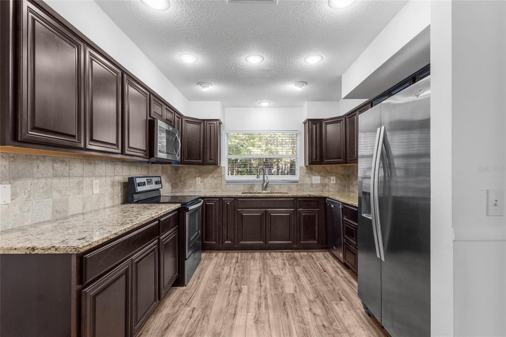 4644 Sawgrass Boulevard New Port Richey, FL 34653 - Photo 6 of 34 a kitchen with stainless steel appliances granite countertop refrigerator a sink dishwasher a stove top oven a refrigerator with wooden cabinets and floor