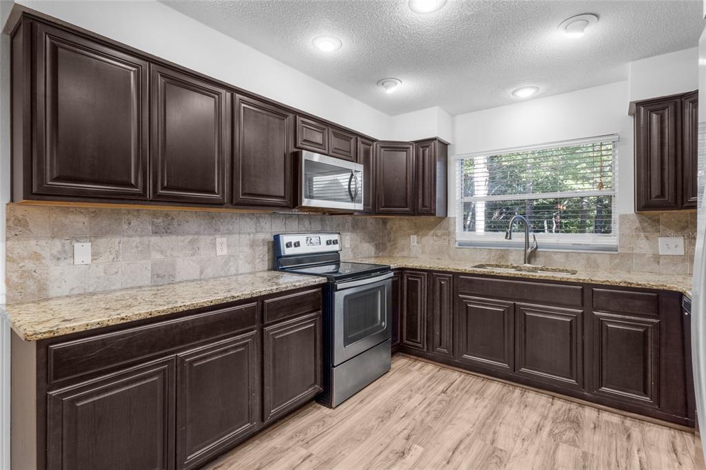 4644 Sawgrass Boulevard New Port Richey, FL 34653 - Photo 8 of 34 a kitchen with stainless steel appliances granite countertop wooden cabinets a stove top oven a sink and dishwasher
