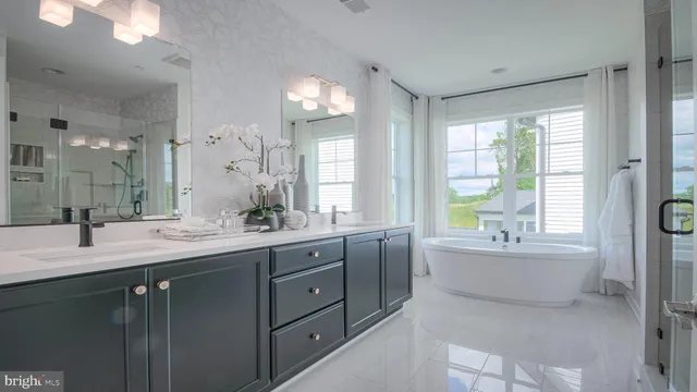 a bathroom with double vanity sinks a large mirror and a bathtub next to a window