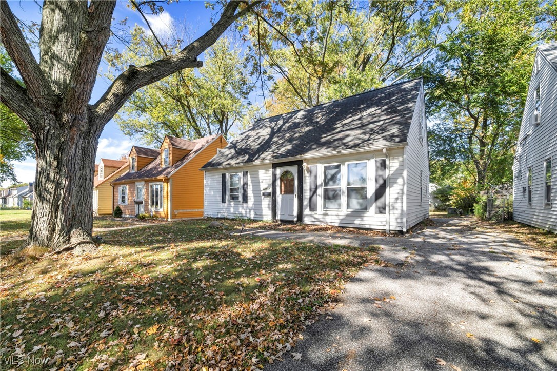 Cape cod home featuring asphalt driveway, a shingled roof, and a front lawn