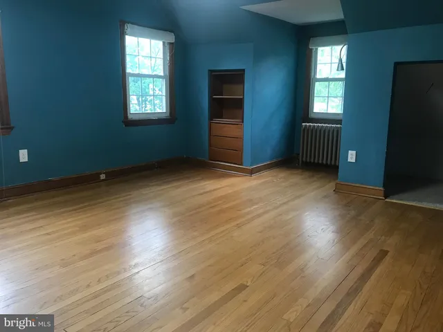 an empty room with wooden floor closet and windows