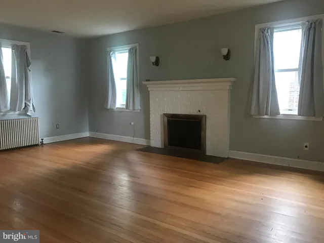 an empty room with wooden floor fireplace and windows
