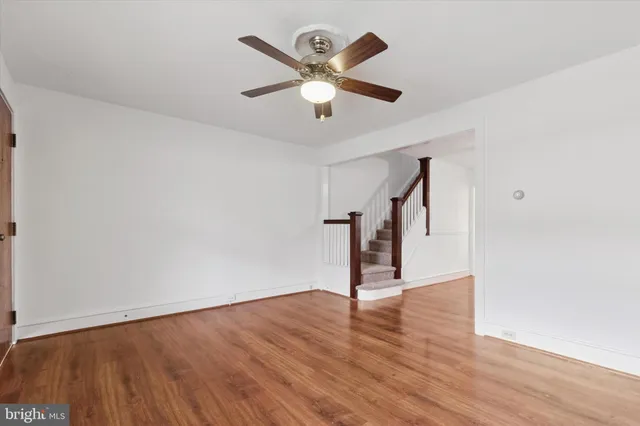 a view of an empty room with wooden floor and a ceiling fan