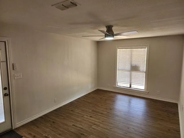 an empty room with wooden floor fan and windows