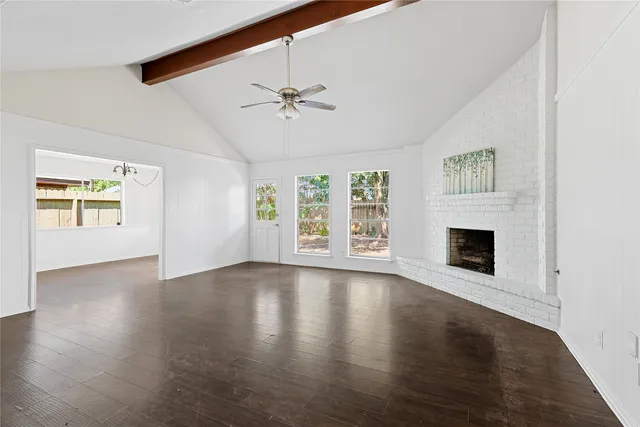 a view of an empty room with wooden floor fireplace and a window