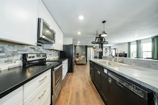 a large kitchen with stainless steel appliances granite countertop a stove a sink dishwasher and a microwave oven with large trees