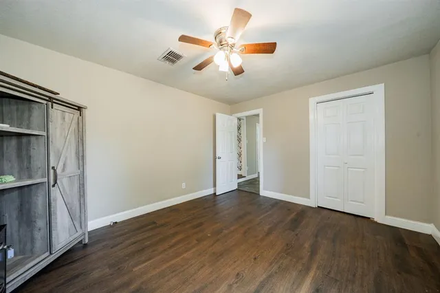 a view of an empty room with wooden floor and a ceiling fan