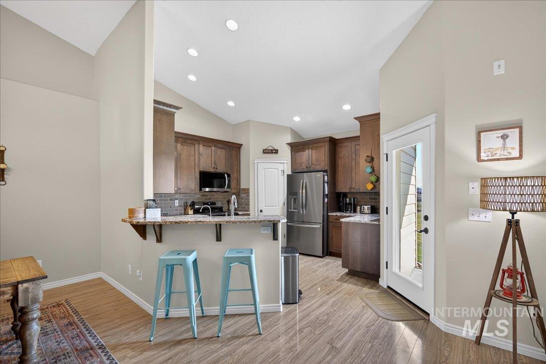 5408 Cassia Road New Plymouth, ID 83655 - Photo 11 of 49 Kitchen with a breakfast bar, decorative backsplash, a peninsula, stainless steel appliances, and light stone counters