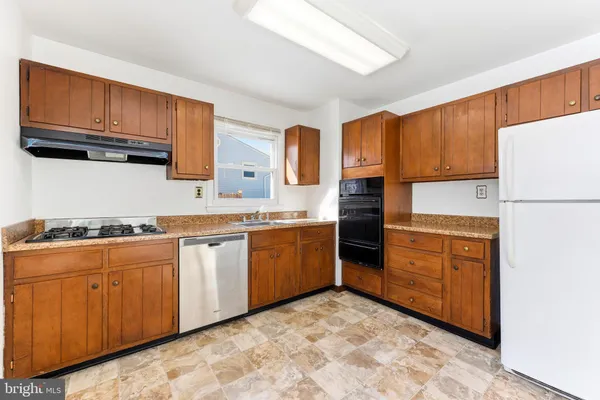 a kitchen with granite countertop a refrigerator stove top oven a sink and dishwasher with wooden cabinets