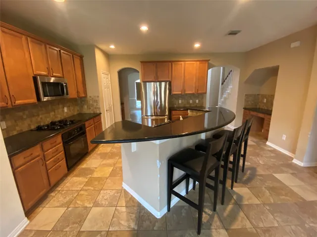 a kitchen with stainless steel appliances granite countertop a stove top oven a sink a dining table and chairs