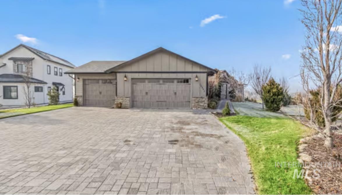 View of front of house featuring board and batten siding, decorative driveway, an attached garage, stone siding, and a front lawn