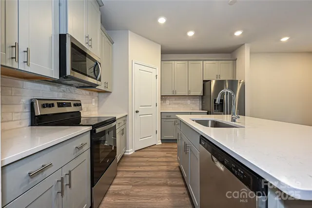 a kitchen with stainless steel appliances granite countertop a sink a stove top oven a refrigerator with white cabinets and wooden floor