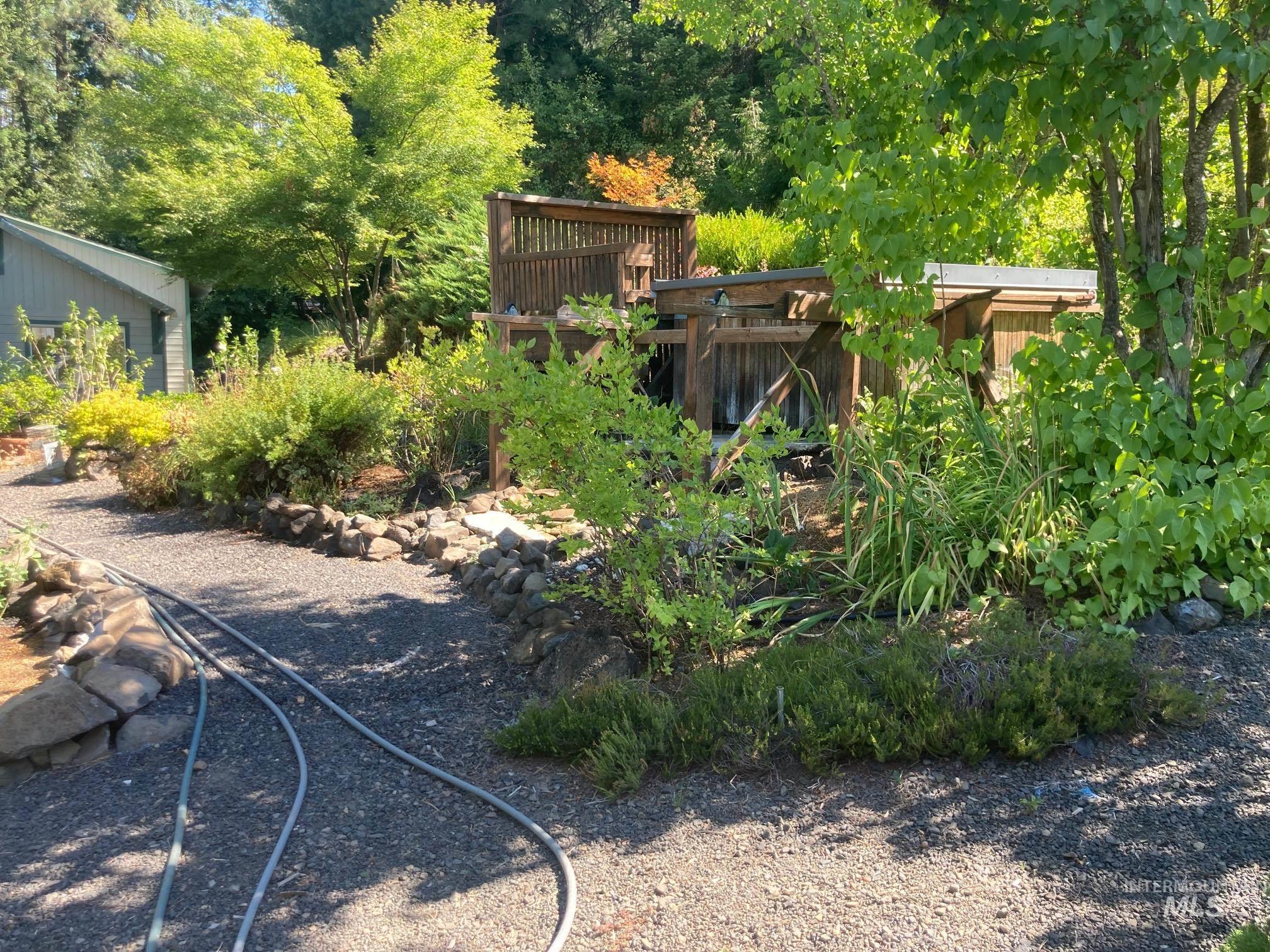 266 Falcon Ridge Road Kooskia, ID 83539 - Photo 36 of 50 Manicured outdoor space featuring a gravel path, established shrubbery, mature trees, a multi-level wooden deck, and a detached wooden structure with a metal roof
