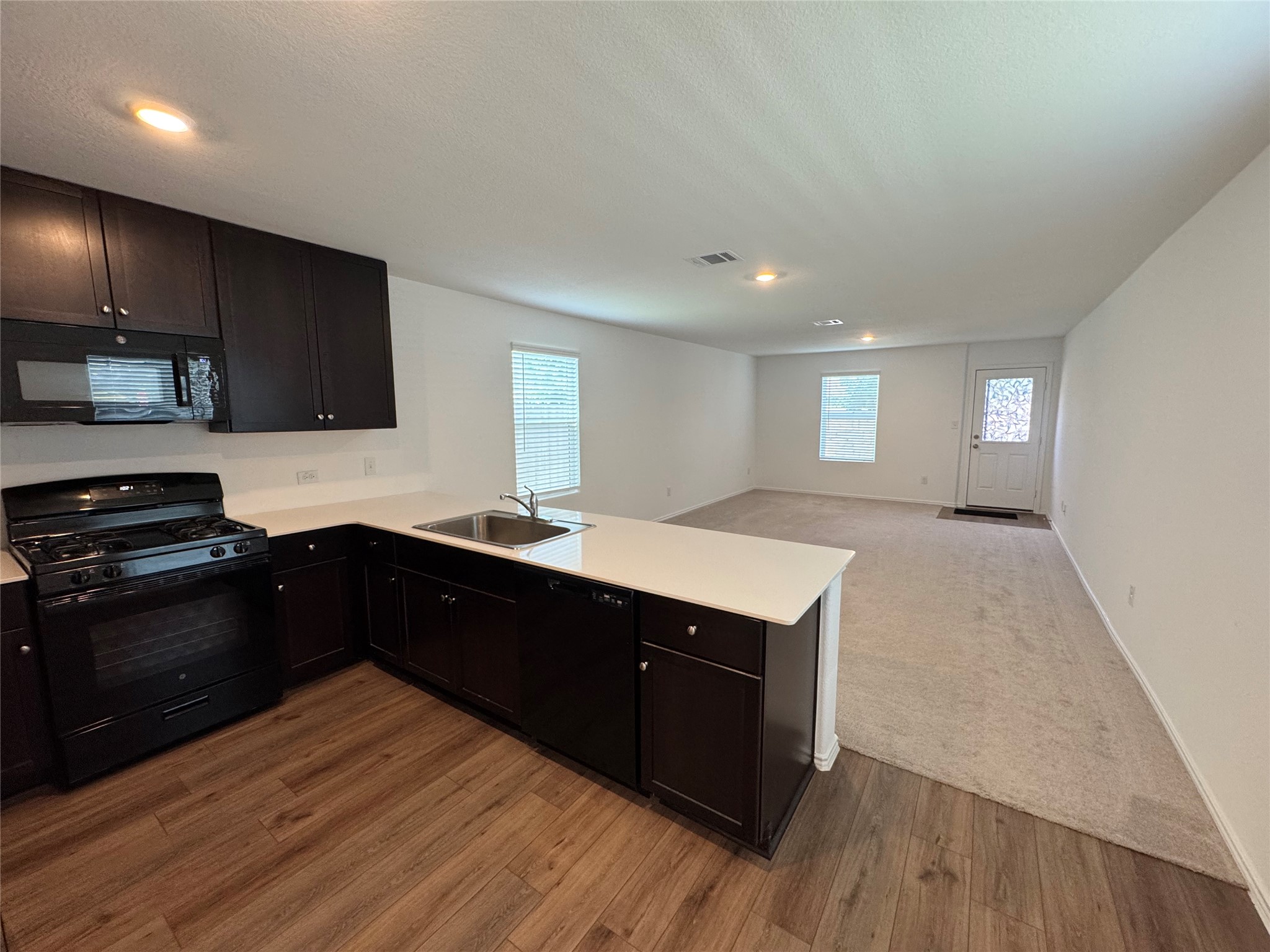 63 Trinity Circle Lockhart, TX 78644 - Photo 4 of 16 An inviting kitchen features a functional island with refrigerator and built-in microwave, pantry, dark cabinetry. and open to the living room