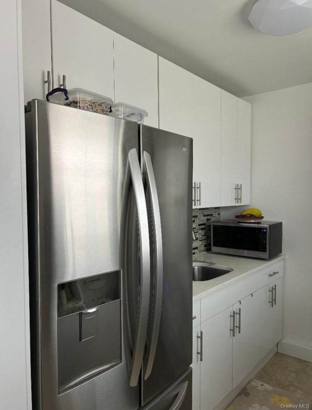 199-05 21st Avenue, Unit 1 Queens, NY 11357 - Photo 9 of 13 a kitchen with metallic refrigerator and white cabinets