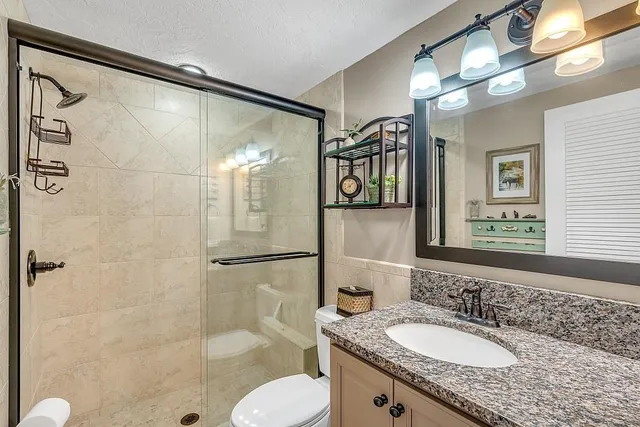 a bathroom with a granite countertop shower sink vanity and mirror