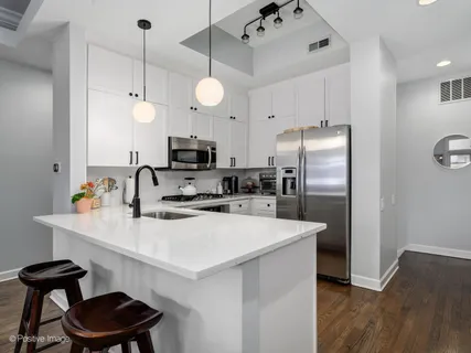 a kitchen with stainless steel appliances a sink a stove a refrigerator and chairs