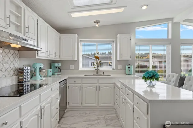 a kitchen with white cabinets a sink a window and white stainless steel appliances