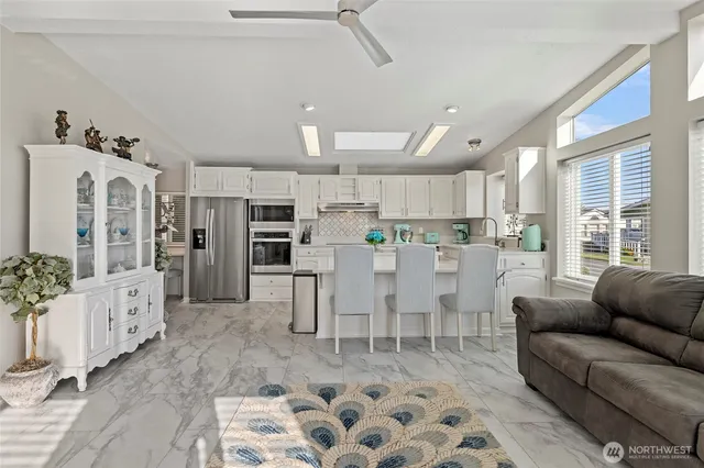 a living room with stainless steel appliances kitchen island granite countertop a refrigerator a sink a dining table and chairs with wooden floor