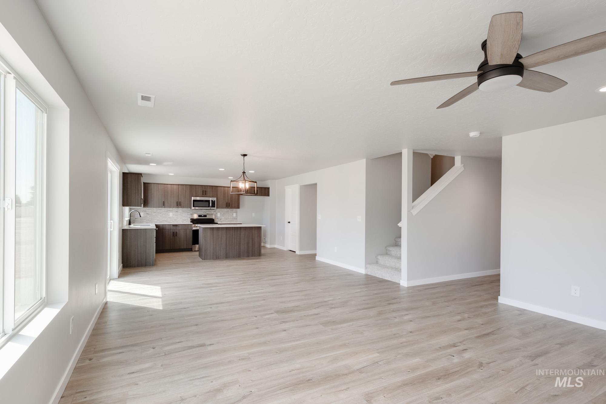 5328 Castleton Avenue Nampa, ID 83686 - Photo 14 of 26 Unfurnished living room with light wood-style flooring, ceiling fan, stairs, recessed lighting, and a chandelier